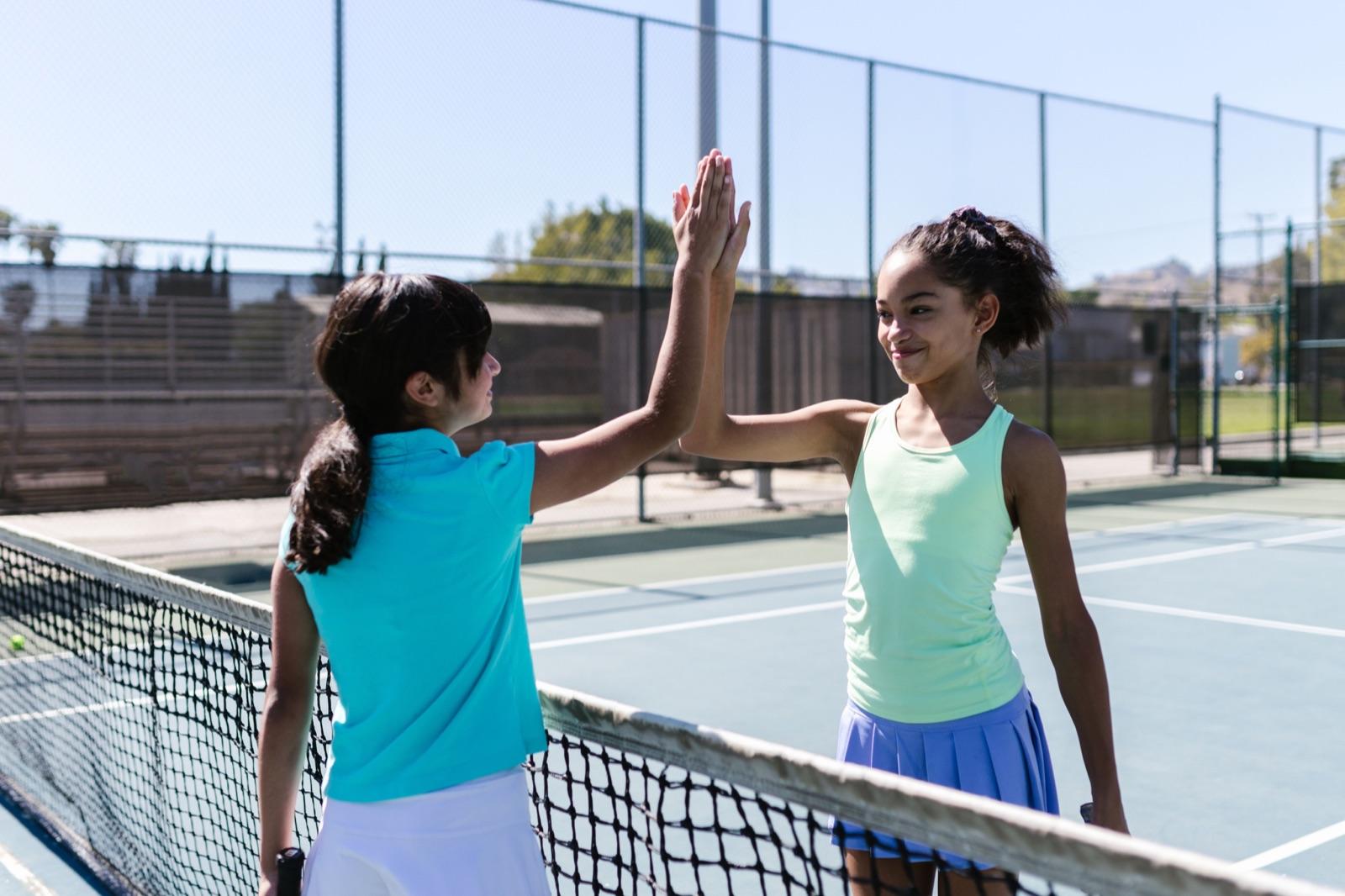 Two girls high-fiving across a tennis net