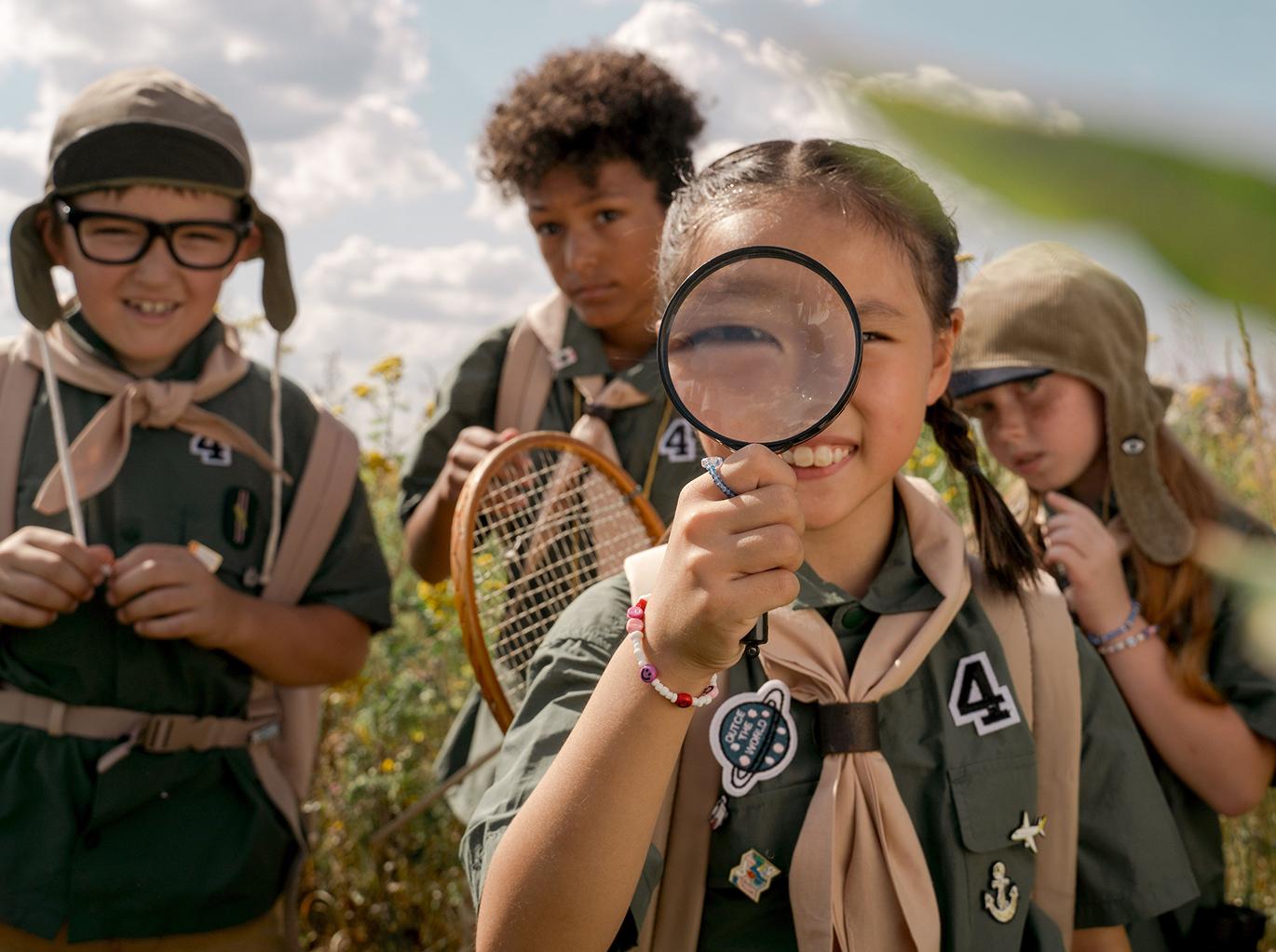 Children outdoors, one looking through a magnifying glass