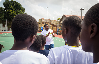 A coach speaking with children on an outdoor court